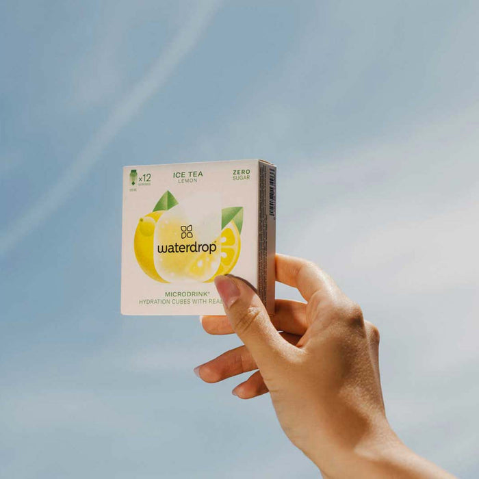 Hand holding a box of waterdrop ice tea against a blue sky background
