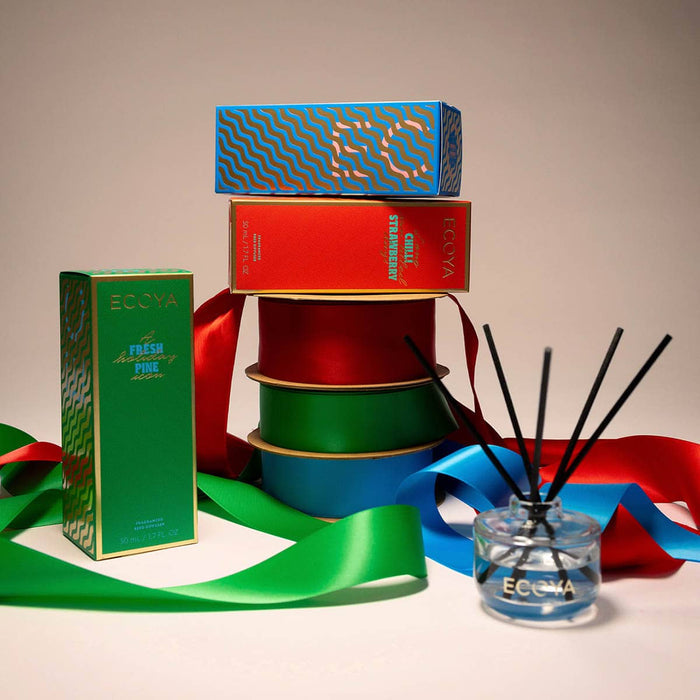 Stack of colourful boxes with a diffuser and ribbons on a beige background.
