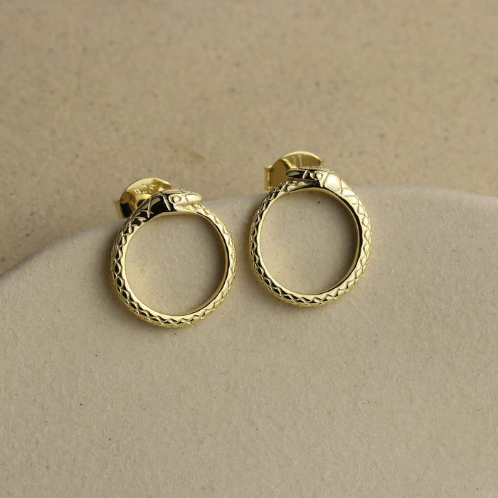 Pair of gold ouroboros hoop earrings on a beige surface