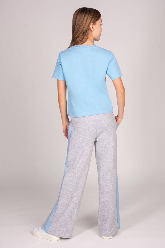 Girl wearing a blue short sleeve t-shirt with matching grey marl wide leg trousers against a plain background.