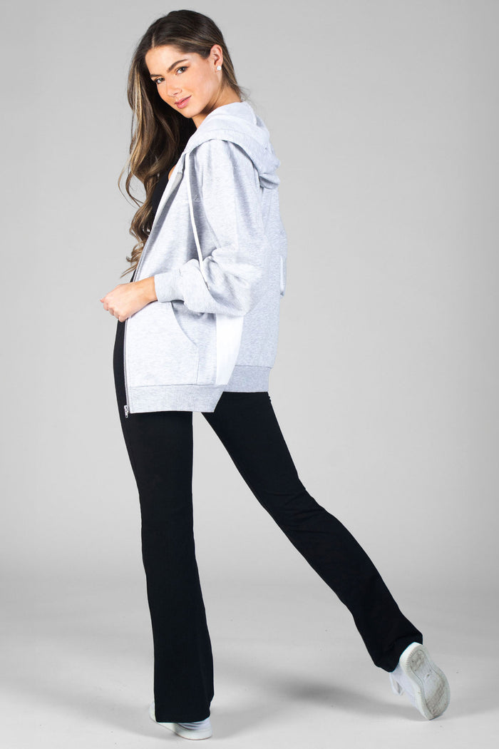 Woman wearing black flared yoga pants with black crop top and grey zip hoodie against a grey background.