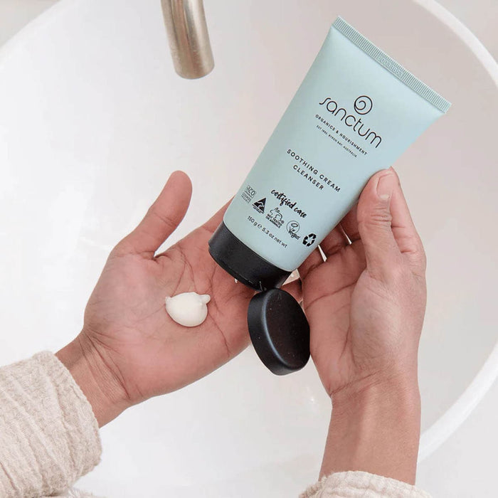 Person holding a tube of Sanctum cream cleanser with a small amount on their palm, against a neutral background.
