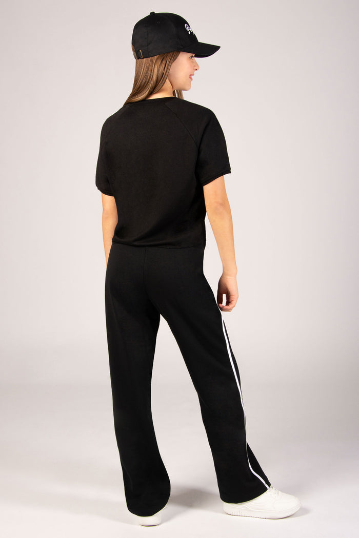 Girl's black wide leg joggers with side panelling in white paired back with black t-shirt and cap.