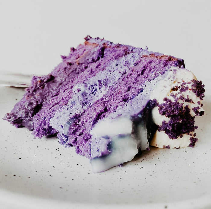 A piece of ube cake with purple layers and vanilla frosting on a plate.