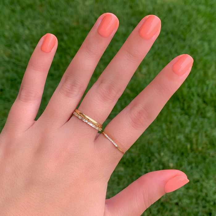 Hand showing Wild & Free | Squoval | Extra Short coral press-on nails with gold rings against green grass background