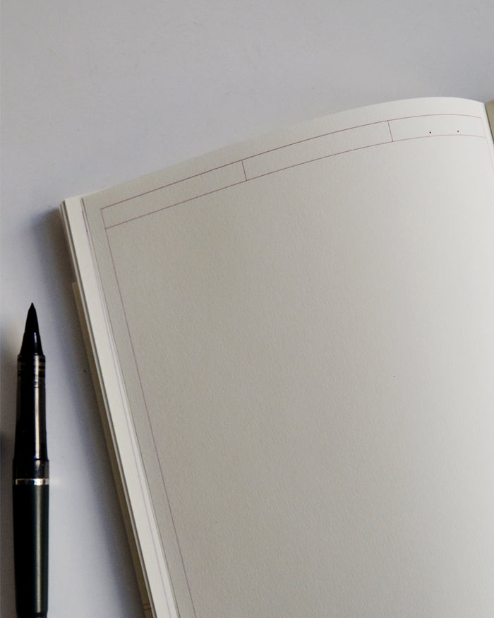 Midori thick journal frame a5 notebook is open with a black pen on the left.