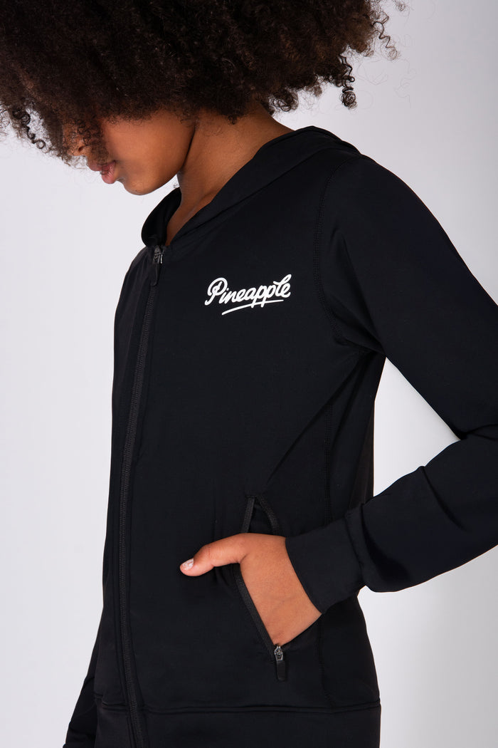Girl wearing a black hoodie with 'Pineapple' logo on a plain background