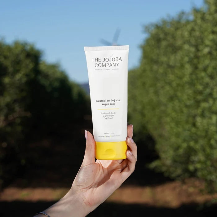 Hand holding a tube of 'The Jojoba Company' Australian Jojoba Aqua Gel with a blurred natural background
