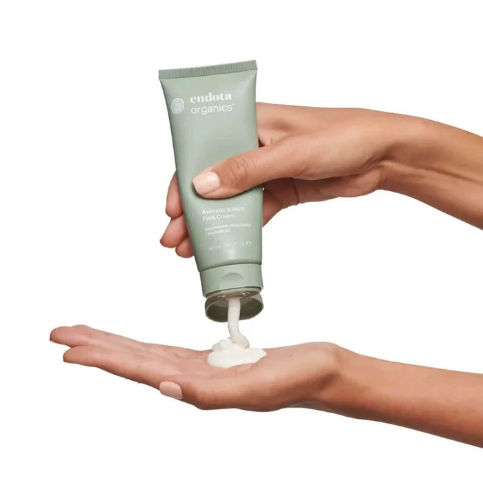 Hand holding a tube of Endota Organics avocado & mint foot cream being squeezed out onto palm.