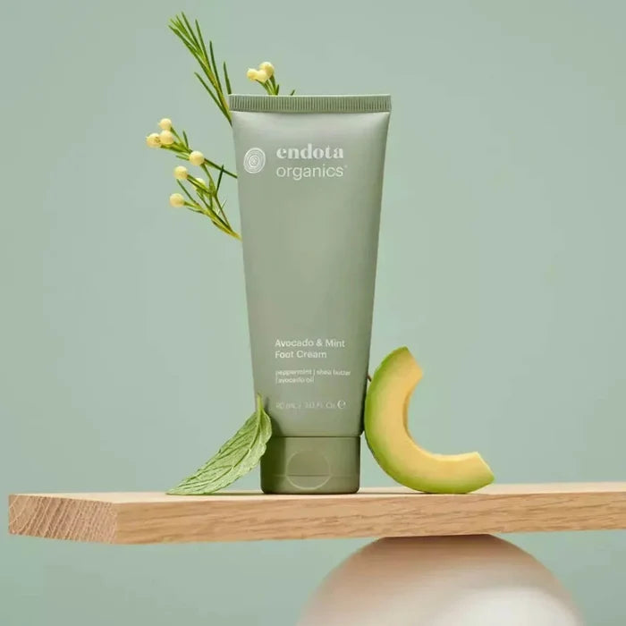 Green tube of Endota Organics foot cream with avocado and mint leaves on a light green background