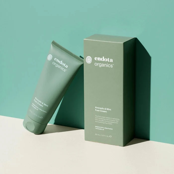 Endota Organics foot cream tube and box on a light beige surface with a teal background