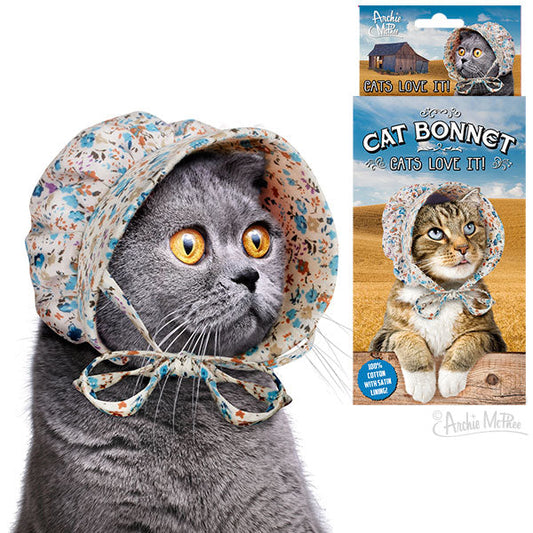 A gray cat wearing a Cat Bonnet, made from 100% cotton in a floral design, sits beside a product package displaying the same delightful image.