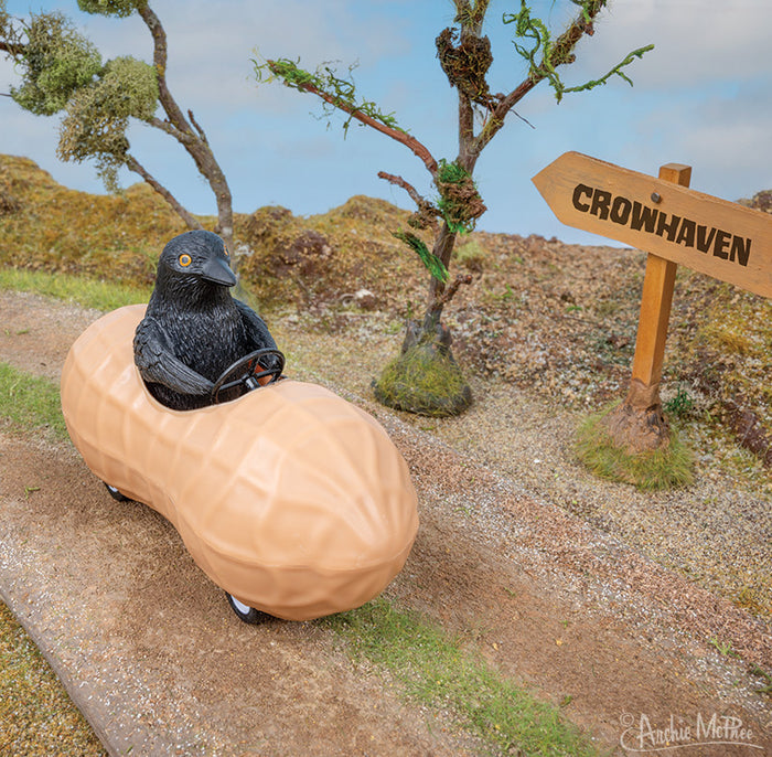A crow in Crow in a Peanut races down the dirt road toward Crowhaven, pulling back the corvid-inspired vehicle for extra speed. Tall trees line the path, and a sign directs him on his journey.