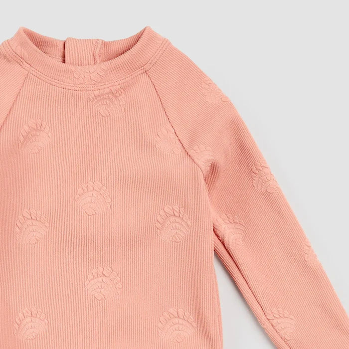 Close-up of embossed seashell ribbed texture on coral Petit Lem kids swimsuit rashguard top
