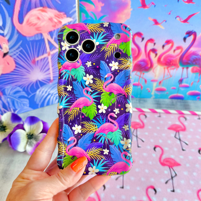 Hand holding the It's Giving Flamingo Wavy Luxe MagSafe iPhone case, showing the purple tropical print with pink flamingos, palm fronds and white blooms.