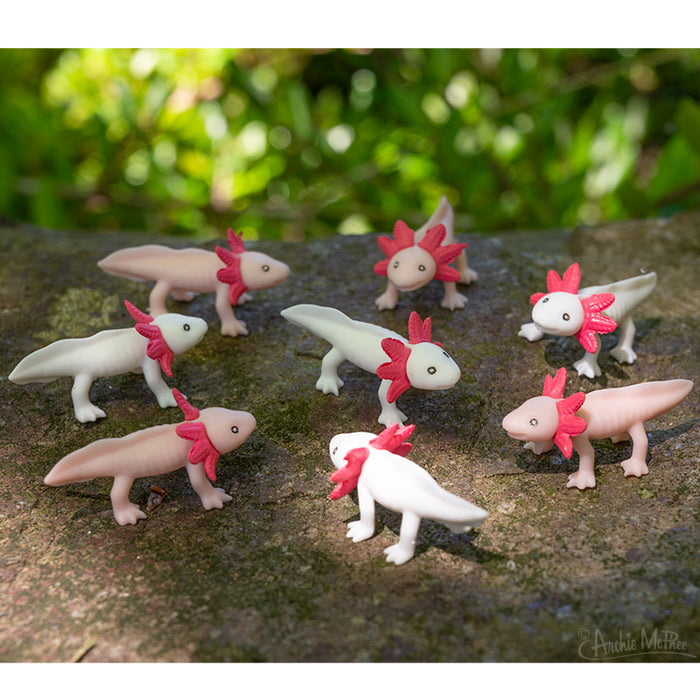 Itty Bitty Axolotls with pink gills are arranged on a mossy rock surface in a garden, made from soft vinyl to achieve a lifelike appearance.