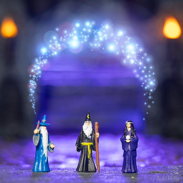 The Itty Bitty Wizards figurines are decorated with shimmering magic on top, contrasted with an enchanting, radiant purple backdrop.