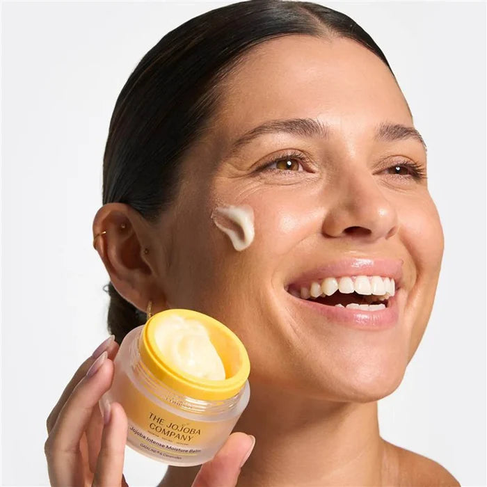 Woman applying cream to her face with an open jar of intense moisture balm next to her cheek.