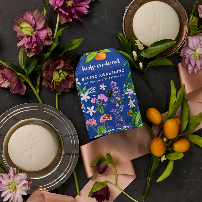 Kale Meleod soap bars and packaging on a dark surface with flowers and fruits.