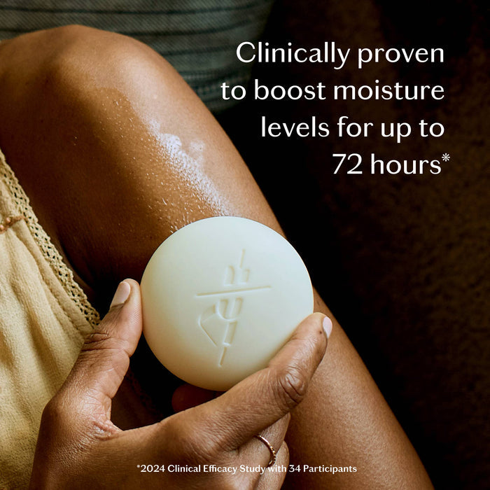 Hand holding a white bar of soap against a person's leg with text about moisturizing benefits.
