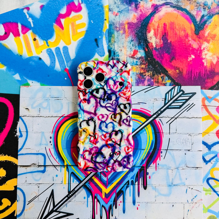 Love Out Loud Wavy Luxe MagSafe iPhone case styled against a street-art heart mural backdrop with a spray-paint arrow.