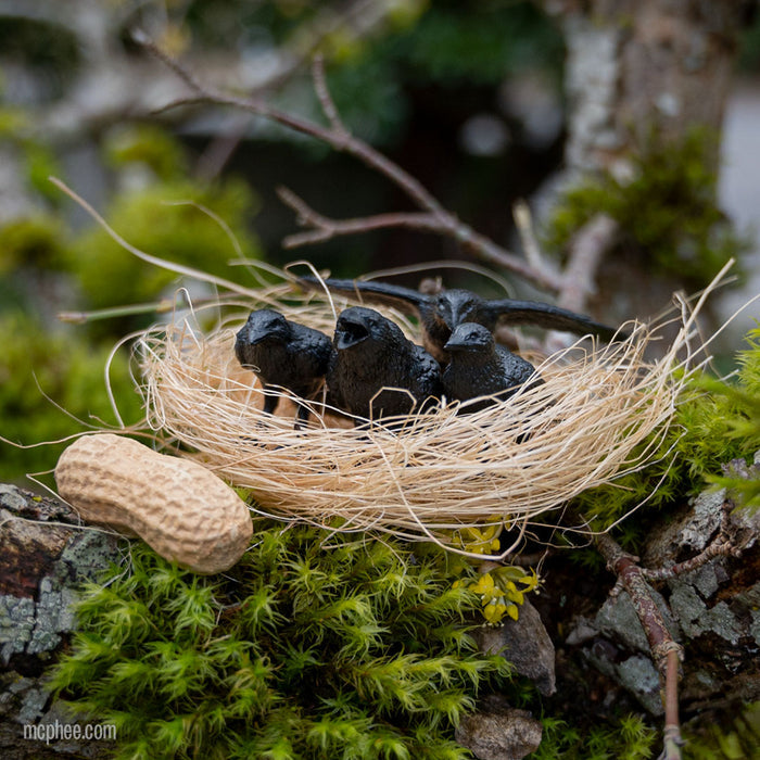 A product called "Murder of Crows" features three decorative crows perched in a nest on a moss-adorned tree branch, situated next to a peanut shell.