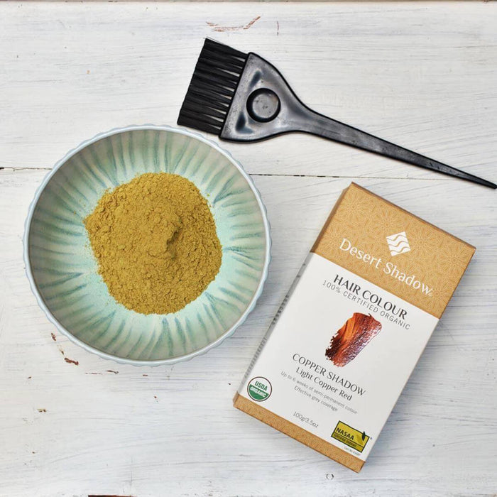 Hair colour powder in a bowl with a brush and Desert Shadow box on a wooden surface.
