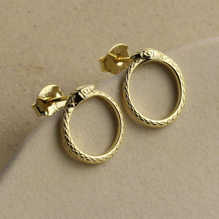 Gold hoop ouroboros earrings on a beige background