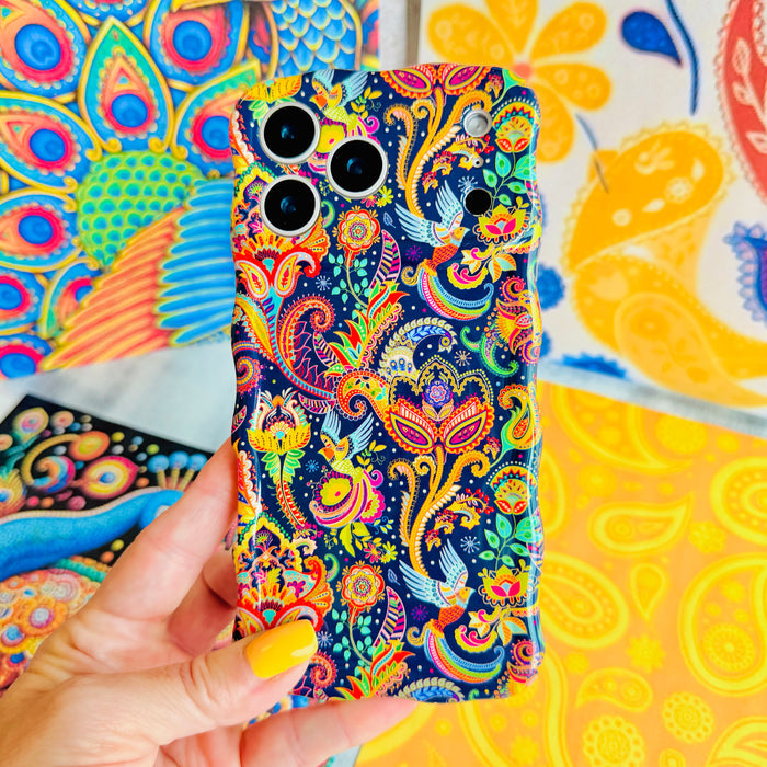 Hand holding the Paisley Birdsong Wavy Luxe MagSafe iPhone case, showing the jewel-toned paisley print with peacock feathers and folk-art birds.