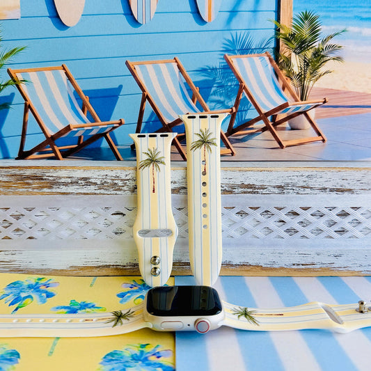 Palm Shore Club silicone Apple Watch band with hand-painted palm trees over soft blue and yellow cabana stripes on an ivory base, shown displayed and worn on Apple Watch against a coastal beach club backdrop.