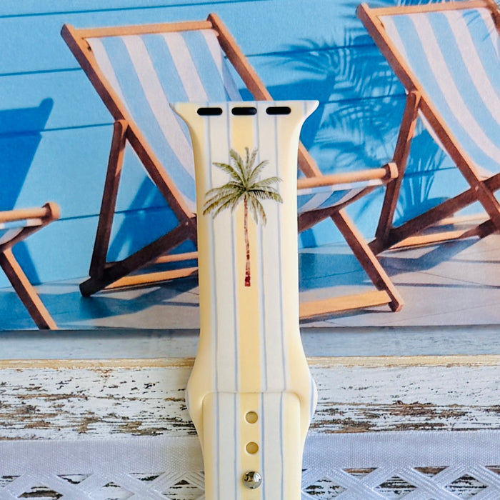 Palm Shore Club silicone Apple Watch band with hand-painted palm trees over soft blue and yellow cabana stripes on an ivory base, shown displayed and worn on Apple Watch against a coastal beach club backdrop.