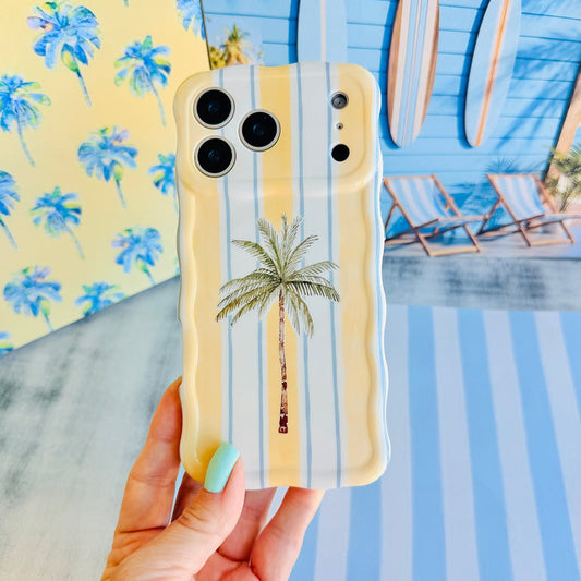 Hand holding the Palm Shore Club Wavy Luxe MagSafe iPhone case, showing the yellow and cream cabana stripe with a single tall palm tree.