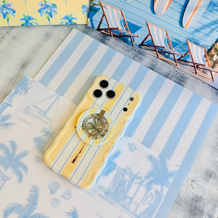 Palm Shore Club Wavy Luxe iPhone case with the matching MagSafe grip ring attached, styled on blue and white striped beach paper.