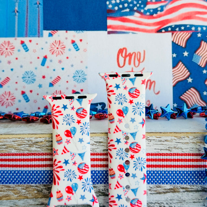 Party In The USA silicone Apple Watch band with fireworks, balloons, cupcakes, flag bunting, and stars in red, white, and blue on a cream base, shown displayed and worn on Apple Watch against a patriotic 4th of July backdrop.