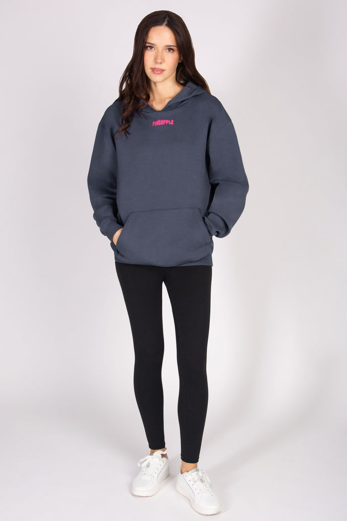 Woman wearing an oversized dark grey hoodie with a pink logo and black leggings on a white background