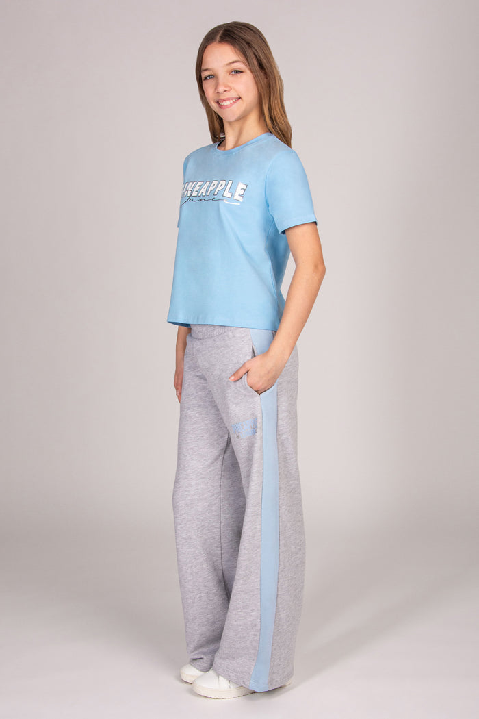Girl wearing a blue short sleeve t-shirt with matching grey marl wide leg trousers against a plain background.
