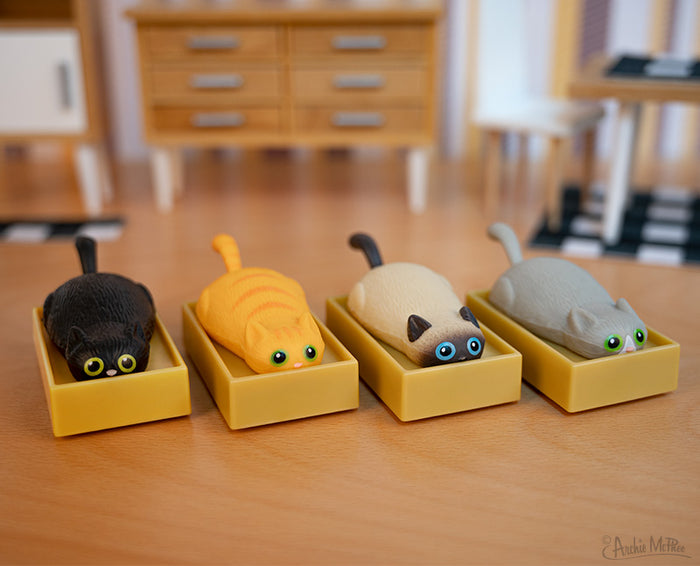 Four Racing Cats in Boxes, vibrant and feline-shaped, rest on a wooden surface with room decor visible in the background.