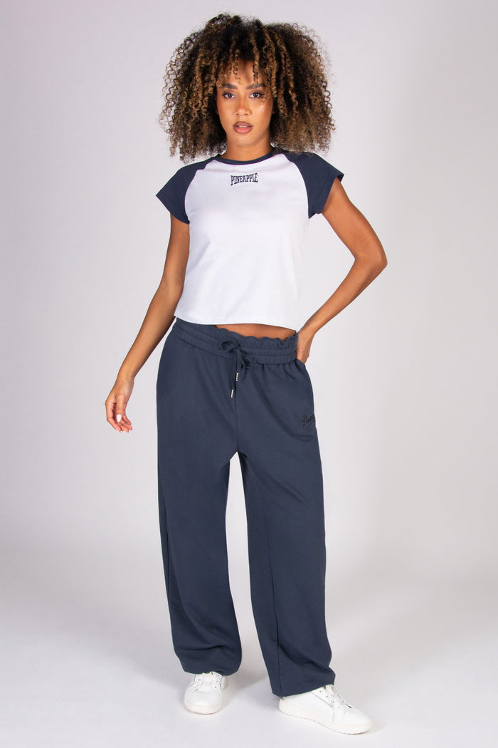 Woman wearing a white t-shirt with dark grey raglan sleeves and oversized dark grey joggers on a plain background