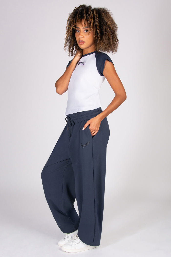 Woman wearing a white t-shirt with dark grey raglan sleeves and oversized dark grey joggers on a plain background