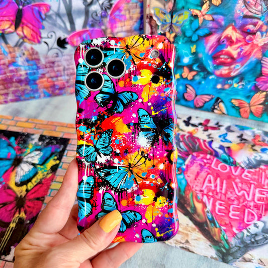 Trendy wavy iPhone case featuring a vibrant street-art collage of electric blue and yellow butterflies over neon pink paint splatters with a high-gloss finish.