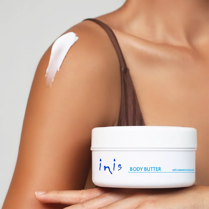 Person applying inis body butter to their shoulder with a plain background