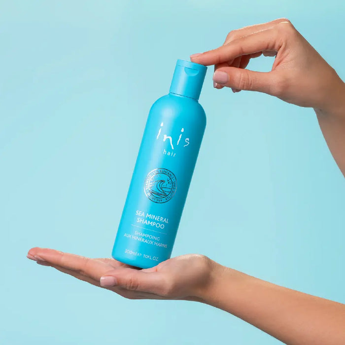 Blue shampoo bottle held by hands against a light blue background