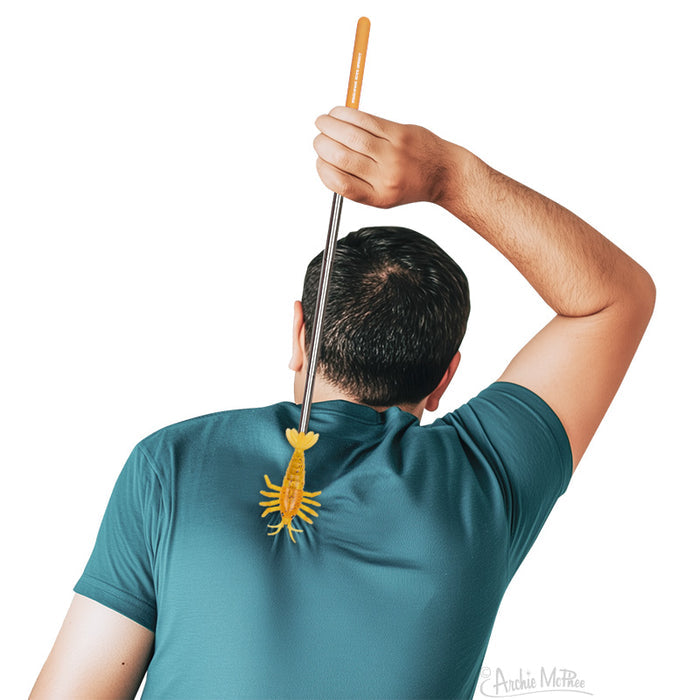 A person uses the Shrimp Back Scratcher, shaped like a yellow bug with an extendable handle, to relieve an itch on their back.