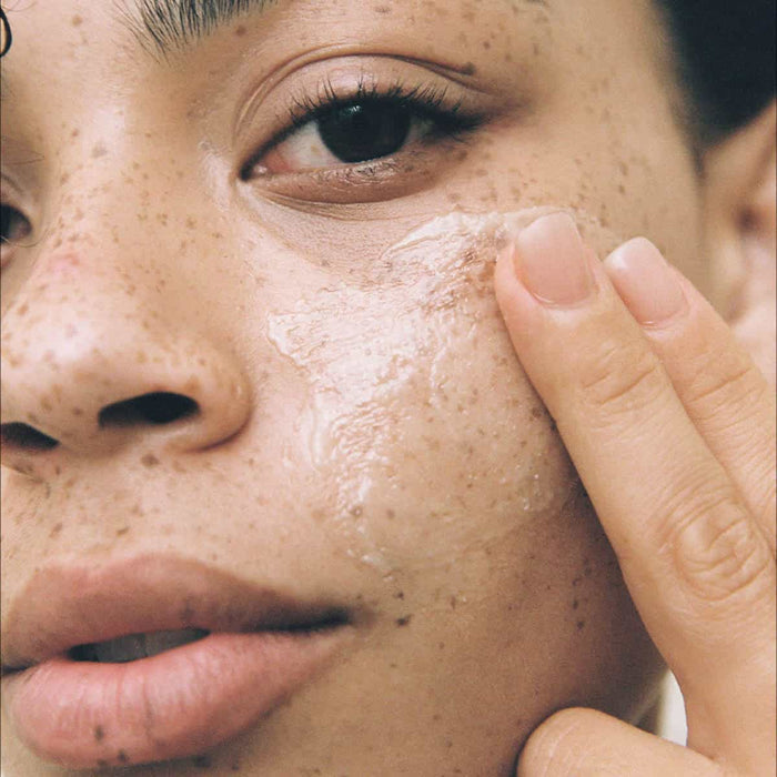 Close-up of a person applying skin butter to their cheek.