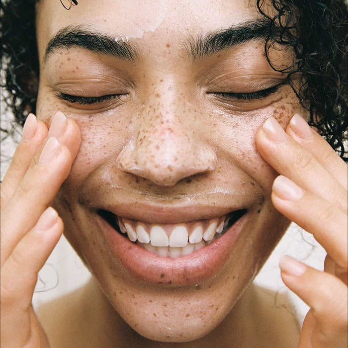 Person smiling while massaging the skin butter cleansing balm into her face.