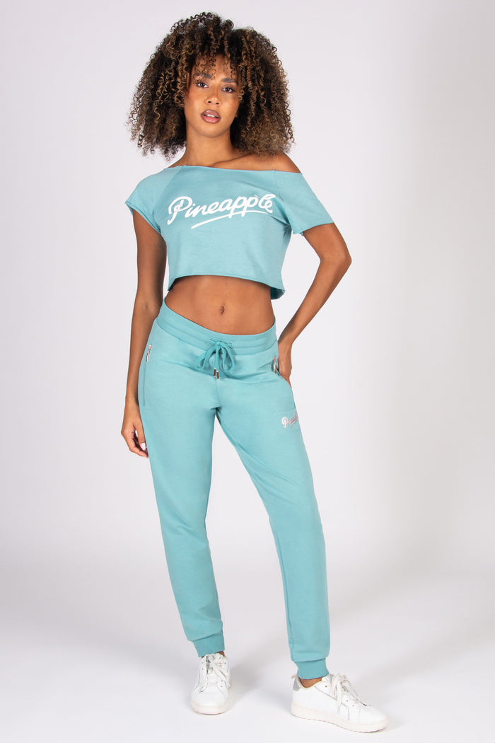 Woman wearing a matching teal crop top and sweatpants set on a white background