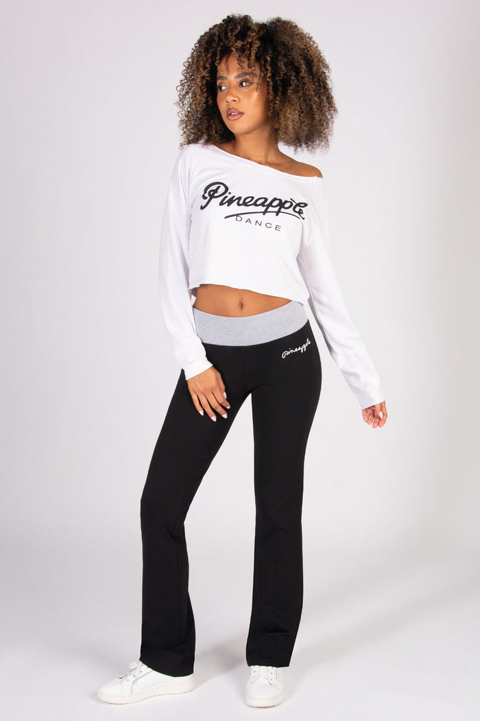 Woman wearing a white long-sleeve top and black flared bootcut trousers with 'Pineapple' branding on a white background