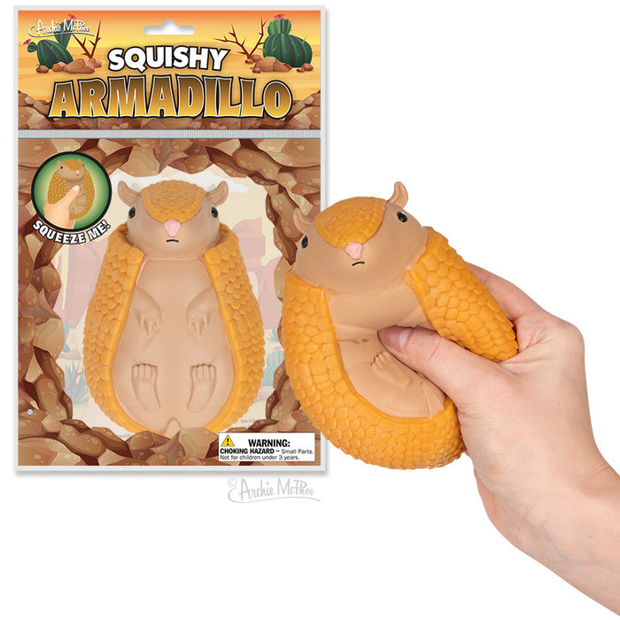 A hand squeezes a yellow Squishy Armadillo toy made of soft rubber, with the packaging visible in the background.