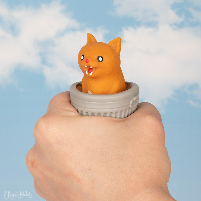 The Surprise Popping Alley Cat ring is worn on a hand, set against a blue sky filled with clouds.