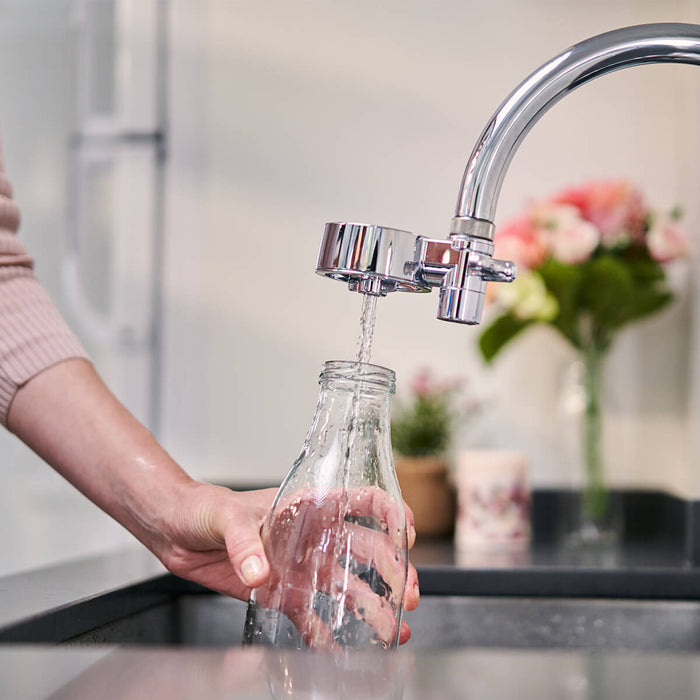 Person filling up a bottle using a Tappwater Tap Water Filter, compact faucet filter that removes impurities.